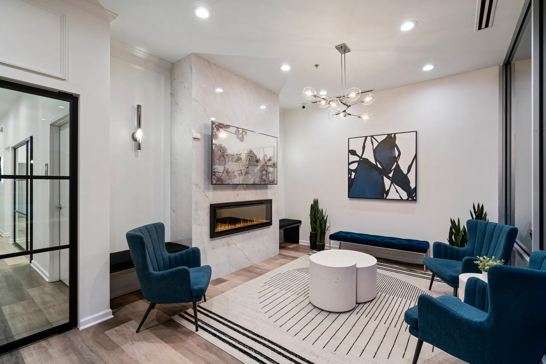 Blue lounge chairs and a pale round table beside a fireplace in the bright waiting room.