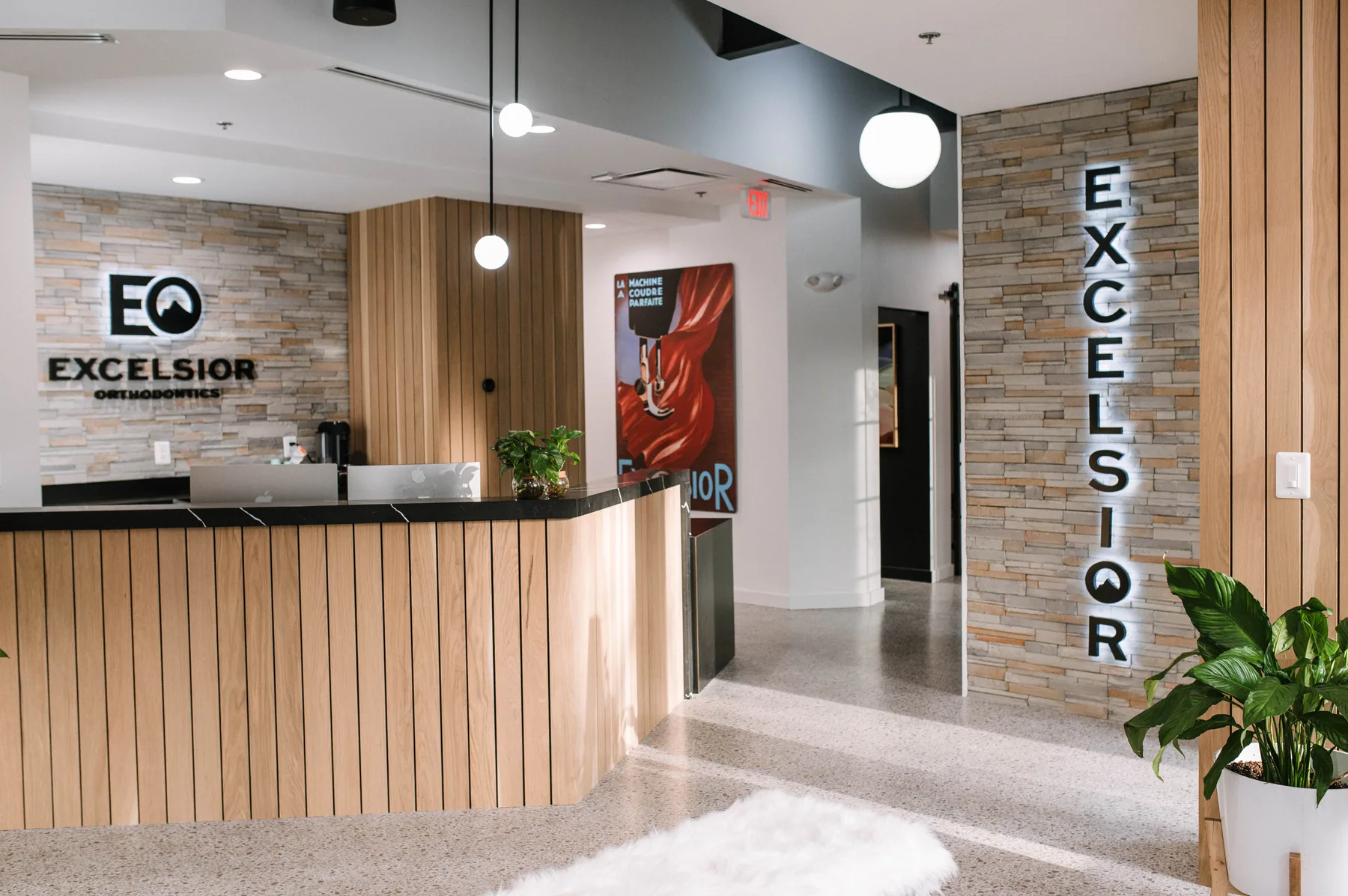 Curved timber reception desk and illuminated Excelsior lettering on stone.