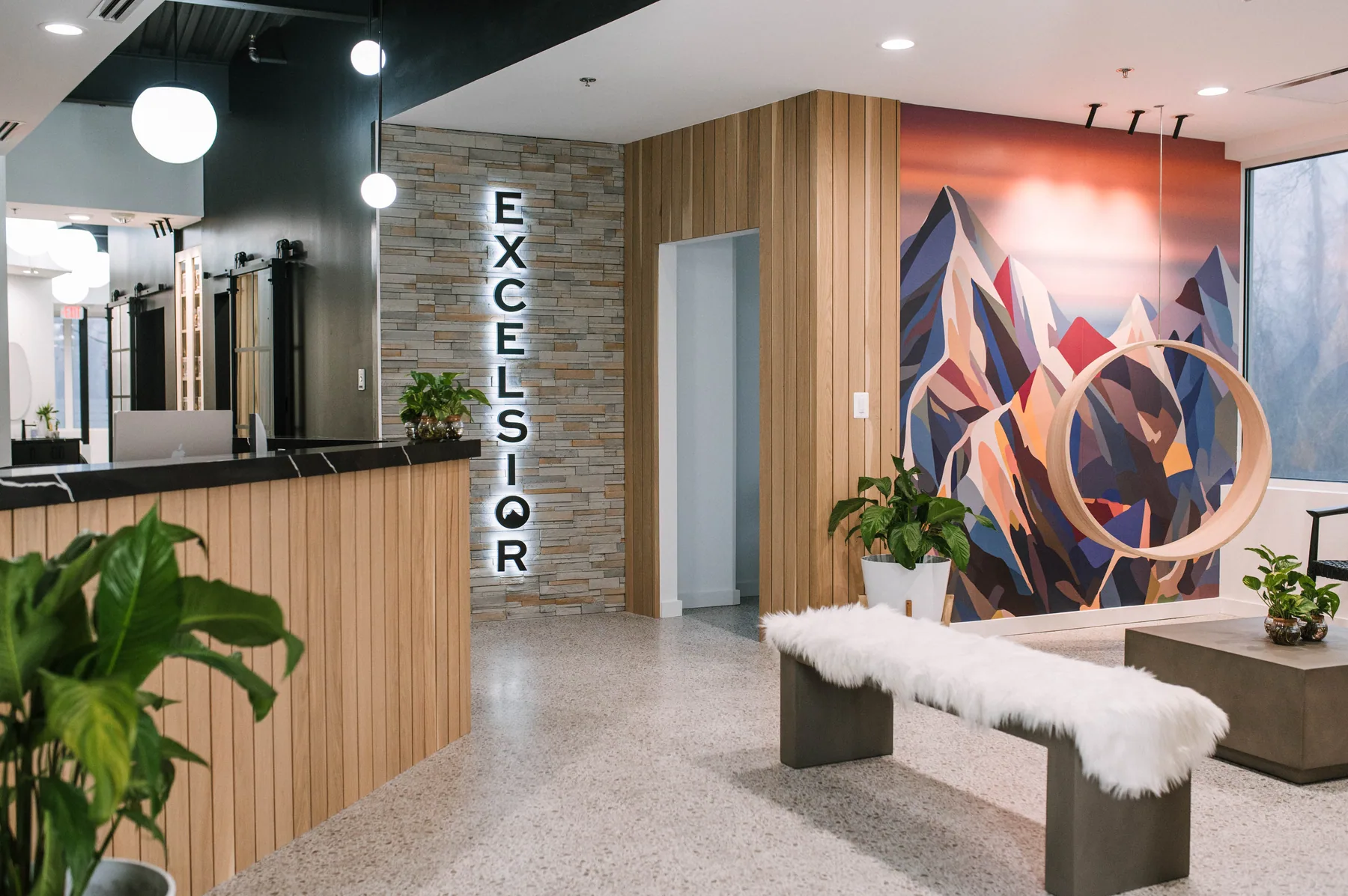 Timber reception and sculptural hanging seat beside a colorful mountain mural.