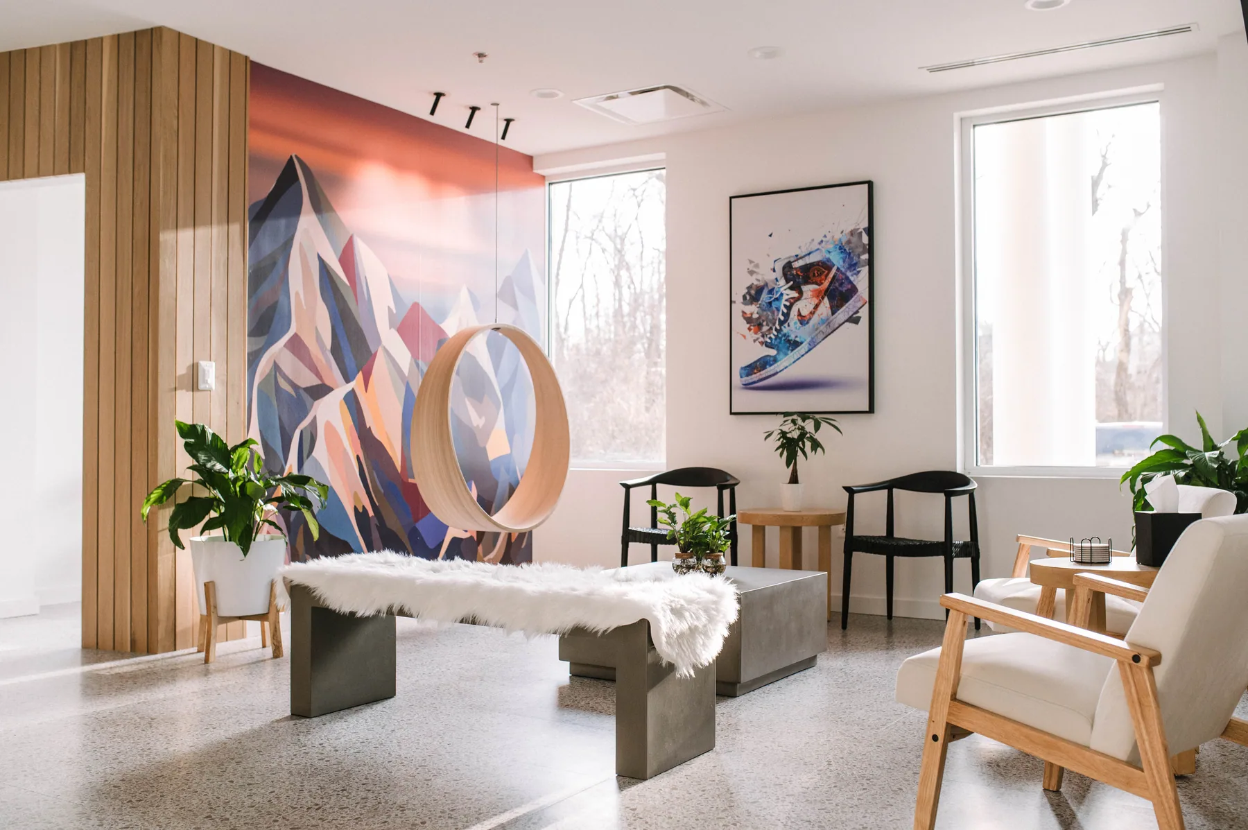 Daylit waiting lounge with timber chairs, a low table and the mountain mural.