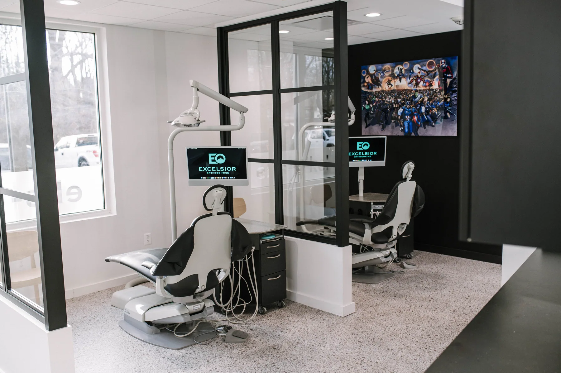 Dental chairs in bright treatment bays divided by black-framed glass.