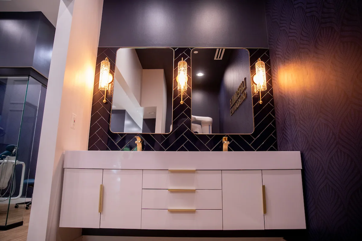 White vanity, navy tiled backsplash and warm pendant lights.