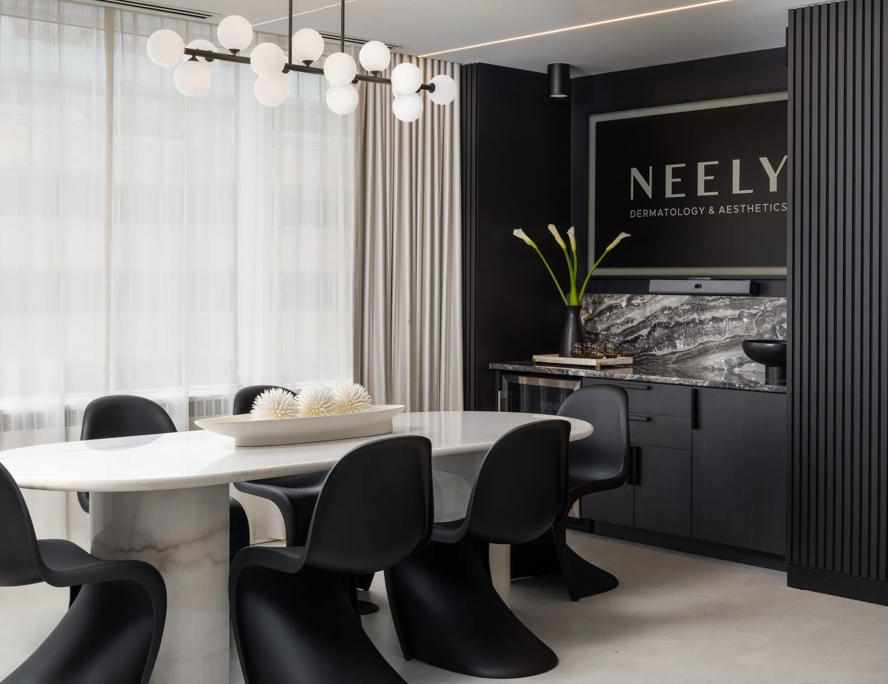 Glazed meeting area with white table, black chairs, branching pendant, and dark cabinetry.