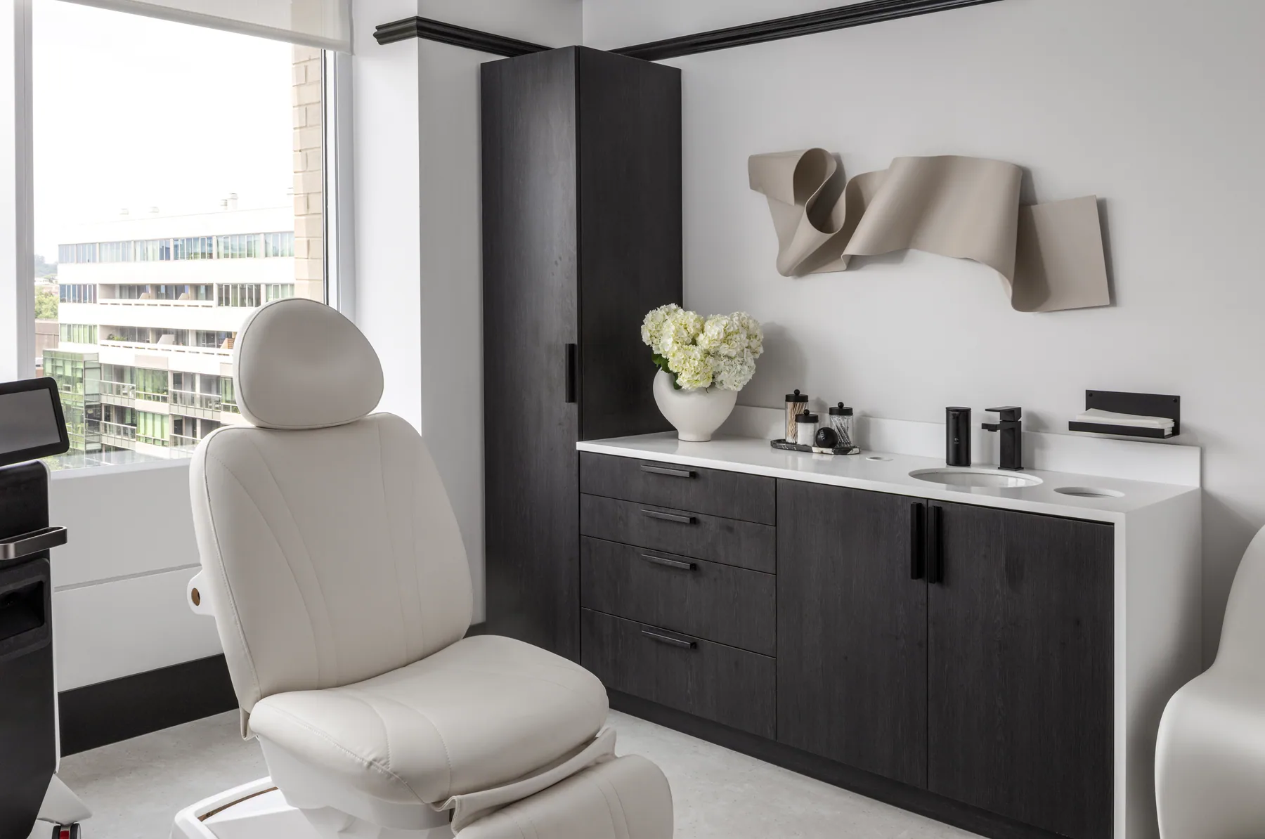 Daylit treatment room with reclining chair and dark cabinetry.